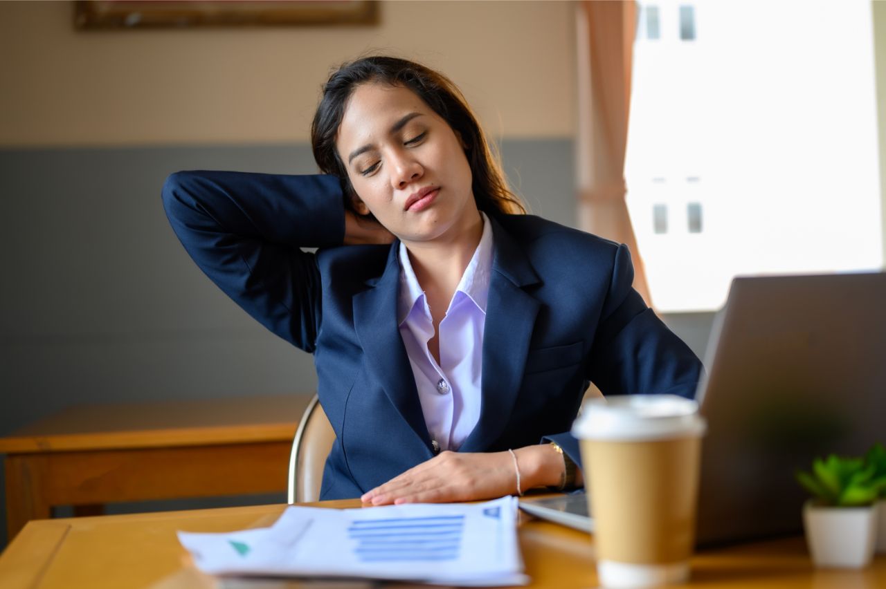 Frau sitzt gestresst am Schreibtisch wegen zu wenig Bewegung